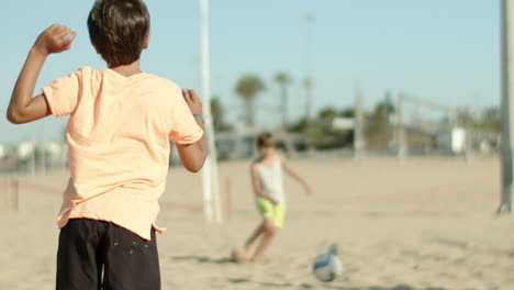 Close-up-shot-of-boy-kicking-ball-to-his-friend-on-sandy-shore